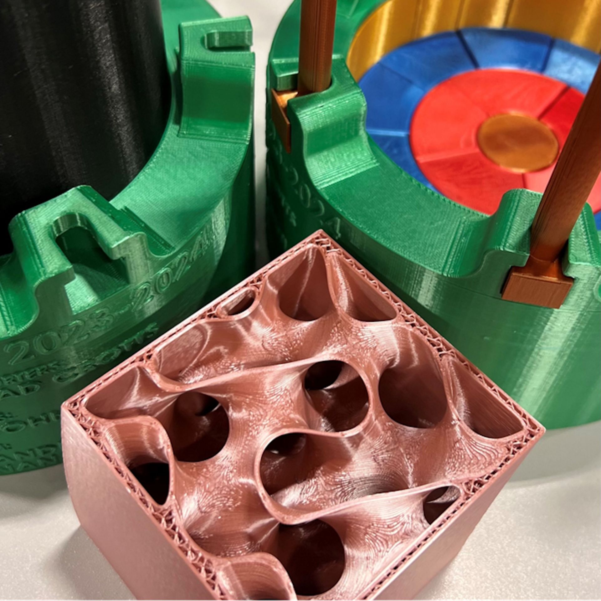 AM工艺制造的1:12比例冲击限制器模型：36块PLA塑料模块（红/蓝/金色）与不锈钢覆层（绿色），前景展示螺旋二十四面体填充结构（粉色）